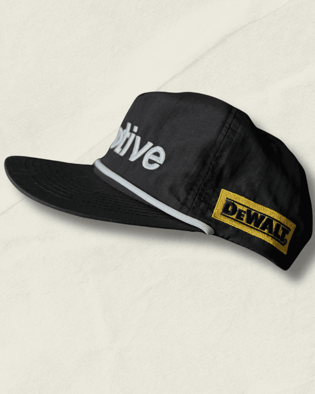 Black Malbon Golf x Motive x DeWalt nylon rope golf hat, front view with raised white motive embroidery, white rope, and yellow DeWalt patches on the sides.