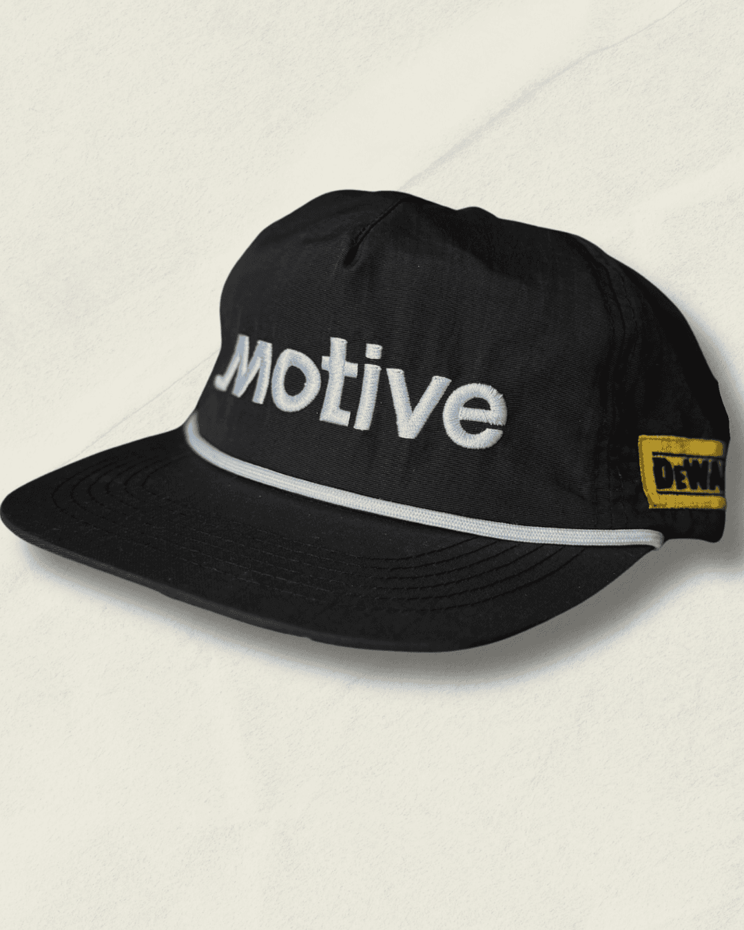 Black Malbon Golf x Motive x DeWalt nylon rope golf hat, front view with raised white motive embroidery, white rope, and yellow DeWalt patches on the sides.
