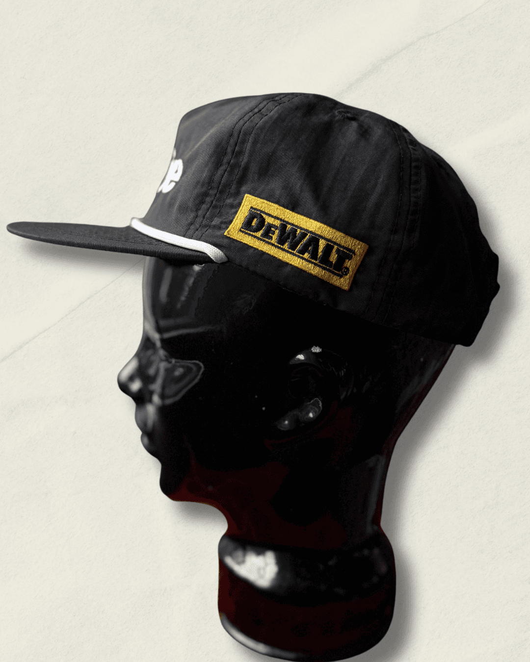 Black Malbon Golf x Motive x DeWalt nylon rope golf hat, front view with raised white motive embroidery, white rope, and yellow DeWalt patches on the sides.