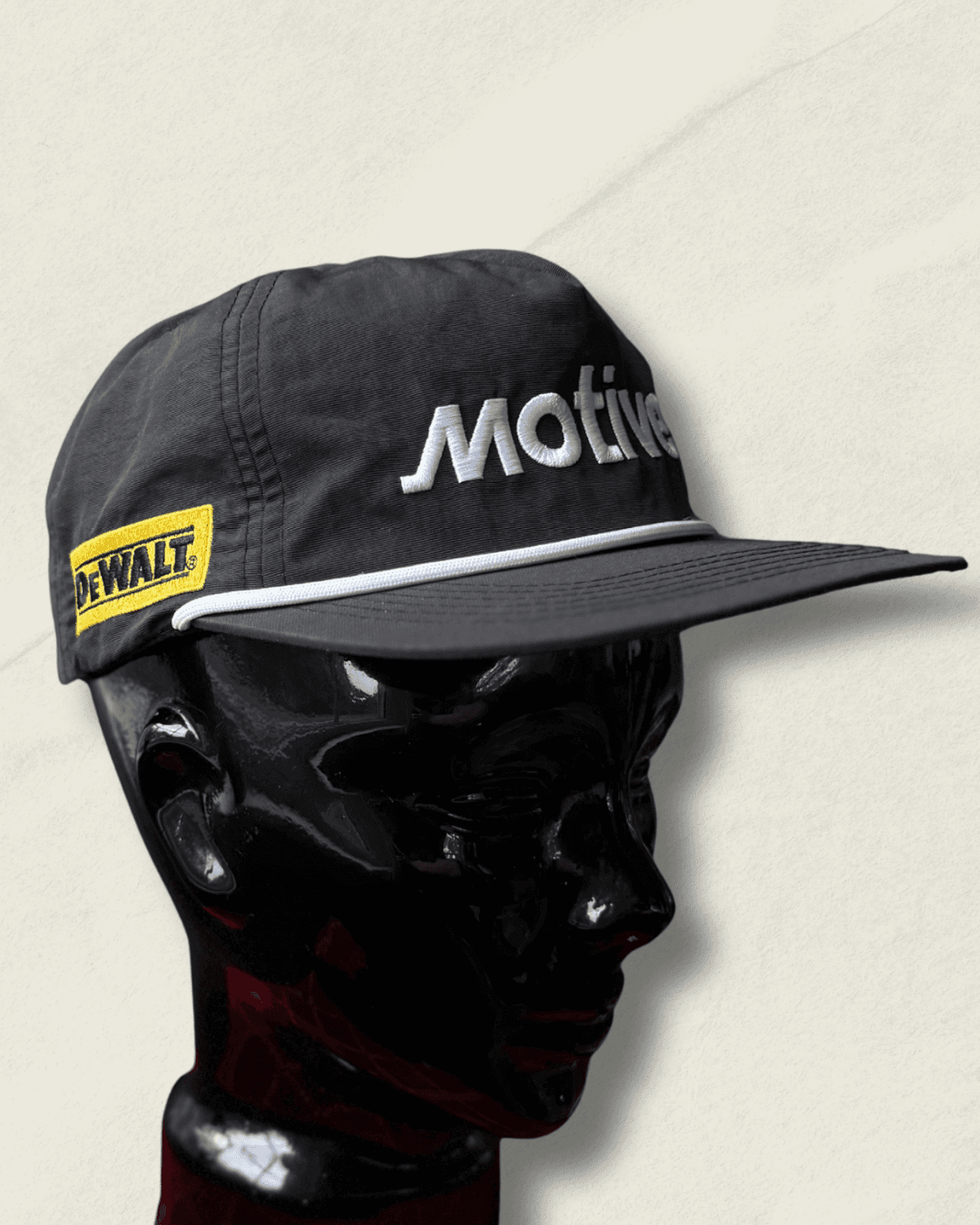 Black Malbon Golf x Motive x DeWalt nylon rope golf hat, front view with raised white motive embroidery, white rope, and yellow DeWalt patches on the sides.